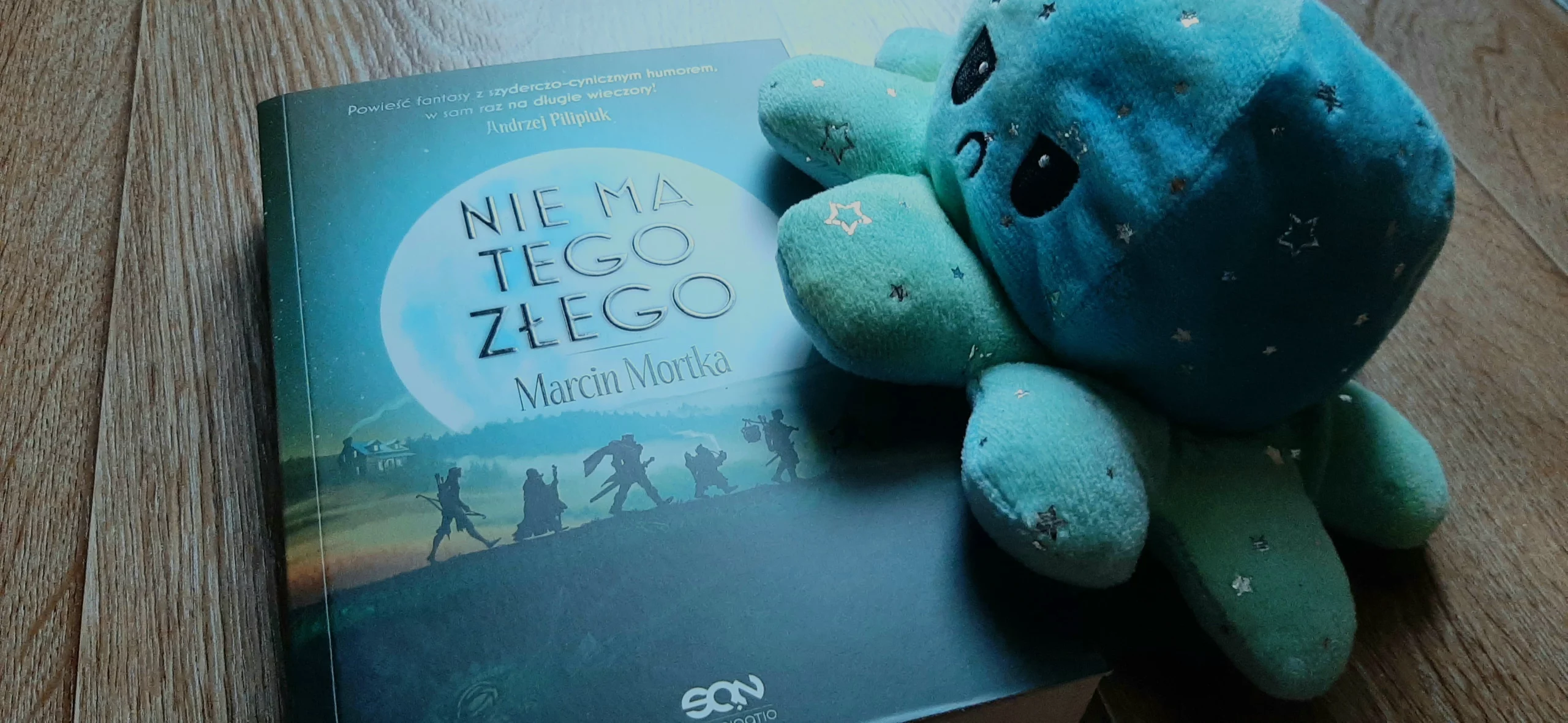 Książka Nie ma tego złego leży na panelach, a zła ośmiornica na nią wchodzi